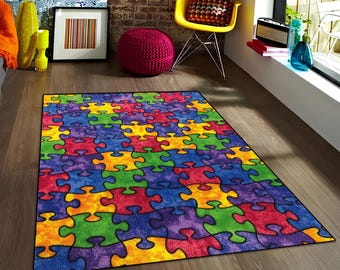 Pode incluir: Um tapete colorido com padrão de peças de quebra-cabeça com peças vermelhas, amarelas, verdes, azuis e roxas. O tapete está sobre um piso de madeira em uma sala com uma cadeira amarela e um pufe vermelho.