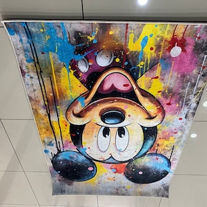 May include: A rectangular area rug featuring an upside-down Mickey Mouse character graphic. The design incorporates a vibrant paint splatter effect with prominent splashes of yellow, blue, pink, and black against a textured, distressed background.