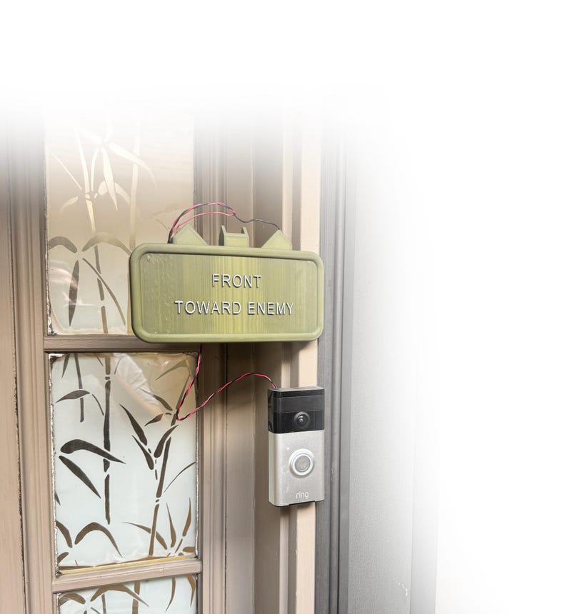 Second installation view of claymore-style novelty doorbell sign beside video doorbell