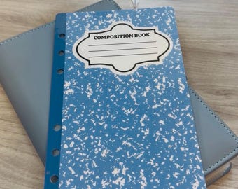 May include: A blue composition book with a white speckled design and the words "COMPOSITION BOOK" in a white label. The book is on top of a blue wallet. The text "budgetingwithcris" is at the bottom.