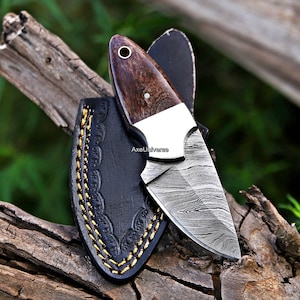 May include: A fixed-blade knife with a Damascus steel blade featuring a wavy pattern, a polished silver bolster, and a dark brown wood handle with a metal lanyard hole. The knife is paired with a black leather sheath featuring yellow stitching.