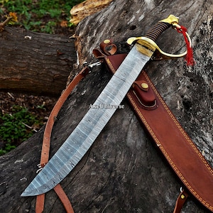 May include: A sword with a patterned Damascus steel blade, a brass handguard, and a black ribbed grip. A red tassel is attached to the pommel. The sword includes a brown leather scabbard with brass hardware and a strap. The text AxeUniverse is visible.