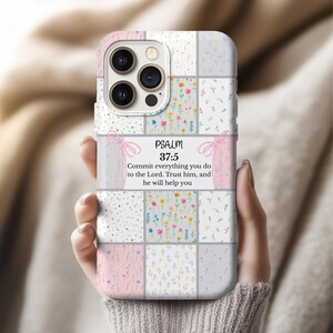 Puede incluir: Una funda de teléfono con un diseño de patchwork con motivos florales y colores pastel. La funda incluye el texto "PSALM 37:5" y un versículo bíblico. La funda está sujeta en la mano de una persona.