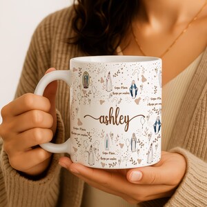Peut inclure: Une tasse en c&eacute;ramique blanche avec une anse noire et le texte "But First, Coffee" en noir gras. La tasse est pos&eacute;e sur une surface en bois. La tasse semble contenir environ 355 ml.