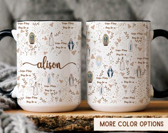 Puede incluir: Taza de cerámica blanca con asa y borde negros, con un patrón repetido de ilustraciones de la Virgen María y el texto "Virgin Mary Pray for us". El nombre "alison" está escrito en marrón.