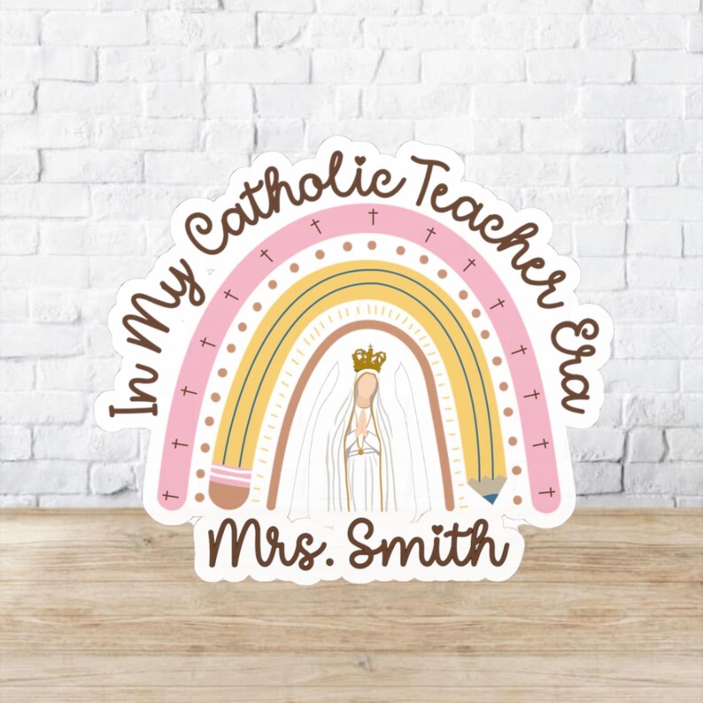 May include: A sticker with a rainbow design and the text "In My Catholic Teacher Era" in a circular layout. The rainbow features pink, yellow, and brown arches, with a depiction of a religious figure at the center. The name "Mrs. Smith" is at the bottom.