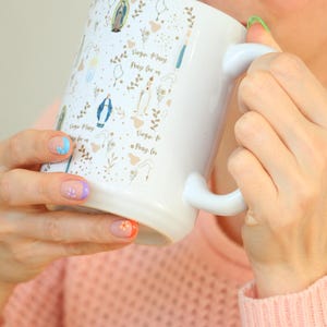 Peut inclure: Une tasse en c&eacute;ramique blanche avec une anse noire et le texte "But First, Coffee" en gras noir. La tasse est pos&eacute;e sur un fond neutre, soulignant son design simple.