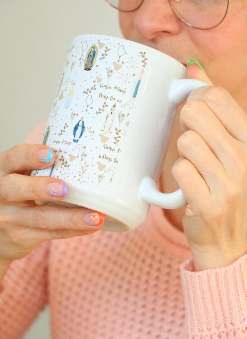 Peut inclure: Une tasse en c&eacute;ramique blanche avec une anse noire et le texte "But First, Coffee" en gras noir. La tasse est pos&eacute;e sur un fond neutre, soulignant son design simple.