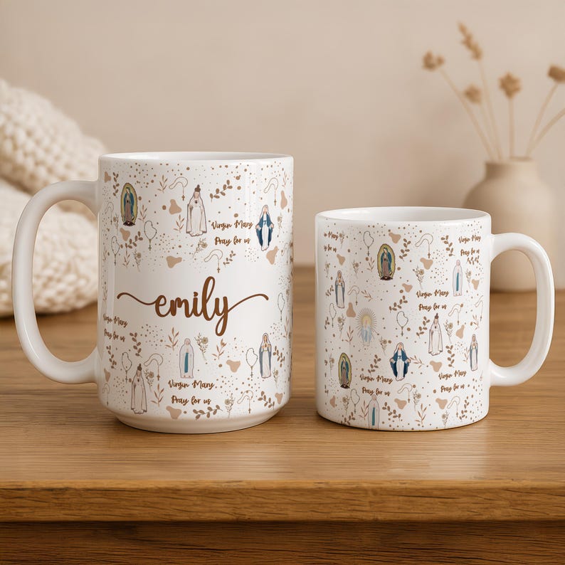 Peut inclure: Deux mugs en c&eacute;ramique blanche avec un th&egrave;me religieux. Les mugs sont d&eacute;cor&eacute;s d'illustrations de la Vierge Marie, d'&eacute;l&eacute;ments floraux et du texte "Virgin Mary Pray for us". Un mug porte le nom "emily" en &eacute;criture cursive.