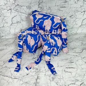 May include: Blue and white patterned travel bag set. The set includes a rectangular bag with a zipper closure and two smaller bags with long fabric ties. The pattern features a repeating design of white shapes on a blue background.