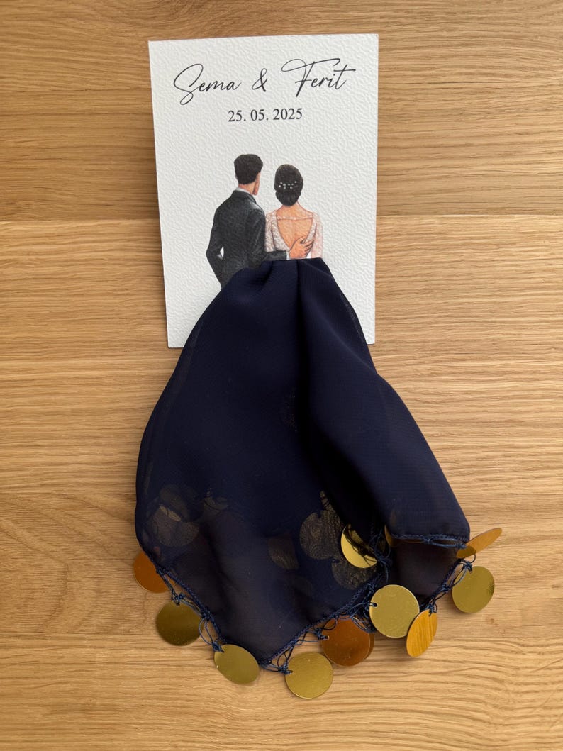 Op de afbeelding: Een witte kaart met de tekst "Sema & Ferit 25.05.2025" en een aquarel-illustratie van een stel in trouwkledij. De kaart is bevestigd aan een donkerblauwe stof met gouden pailletten.