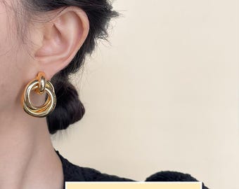 Op de afbeelding: Gouden oorbellen met dubbele cirkel en een geknoopt ontwerp.