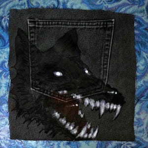 May include: A dark gray denim patch featuring a menacing wolf illustration. The wolf's eyes glow white, and its fangs are bared. The design is centered on a denim pocket, creating a unique, edgy aesthetic.