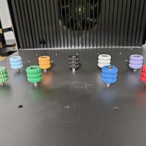 May include: Nine different colored plastic knobs with a textured surface. The knobs are arranged in a circle on a gray surface. The text "Microcenter PC" is visible in the center of the surface.