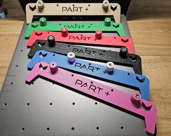 Puede incluir: Colección de herramientas metálicas coloridas, cada una con el texto "PART +" y perillas ajustables. Las herramientas son beige, verde, rojo, negro, azul y rosa, dispuestas sobre una superficie gris con fondo de madera.