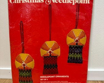 May include: A Bucilla Christmas Needlepoint kit, No. 60341, featuring three ornaments with a red, green, and yellow color scheme. The kit includes single mesh interlock 100% cotton canvas, 100% acrylic Persian Crown yarn, full stitching instructions and a way to make the needlepoint ornaments.