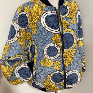 May include: A blue and gold bomber jacket with a zipper closure and a floral pattern featuring clock faces.