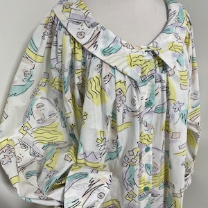 May include: A white button-up shirt with a large collar and long sleeves. The shirt has a colorful abstract print featuring faces and geometric shapes in shades of yellow, green, purple, and pink.