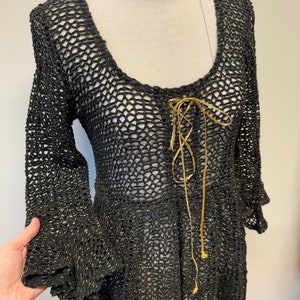 May include: Black crochet top with gold thread detailing and a tie at the neckline.