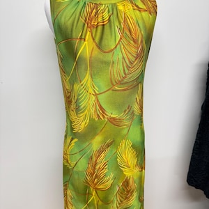 Puede incluir: Vestido vintage sin mangas con cuello alto. El vestido presenta un fondo verde vibrante con un patrón repetido de formas amarillas y marrones en forma de pluma. El vestido se exhibe en un maniquí.