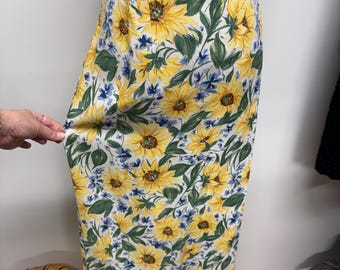 Puede incluir: Falda larga y floral con un vibrante estampado de girasoles. La falda presenta grandes girasoles amarillos con hojas verdes y detalles azules sobre un fondo blanco. La falda es entallada y de cintura alta.