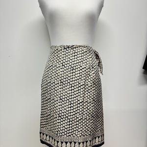 May include: A black and white floral wrap skirt with a black and white patterned border. The skirt is made of a lightweight fabric and has a tie closure at the waist.