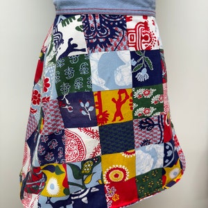 May include: A patchwork skirt with a blue denim waistband. The skirt is made of various fabrics with different patterns, including floral, geometric, and animal prints. The colors are bright and vibrant, including red, blue, yellow, green, and white.