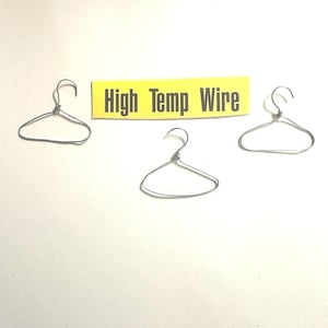 May include: Three small, silver wire hangers are arranged on a white surface. A yellow rectangle with the words "High Temp Wire" in black text is positioned above the hangers. The hangers are simple in design, with a hook and a triangular body.
