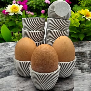 May include: Four brown eggs in grey, textured egg cups. The egg cups are stacked in a pyramid shape.