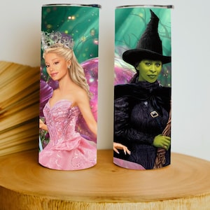 May include: Two stainless steel tumblers with fantasy-themed artwork. One features a woman in a pink dress and crown, the other a green-skinned witch in a black hat and cape. Both have a green and purple background.