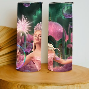 May include: A stainless steel tumbler featuring a fantasy illustration. The design includes a woman in a pink dress and tiara, holding a wand, with a castle and bubbles in the background. The tumbler is cylindrical and has a silver lid.