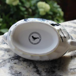 May include: White ceramic teapot with a bird design and black text. The bottom of the teapot has a circular stamp that reads "Dishwasher & Microwave Safe" and "Made in China Fabriqu&eacute; en Chine".