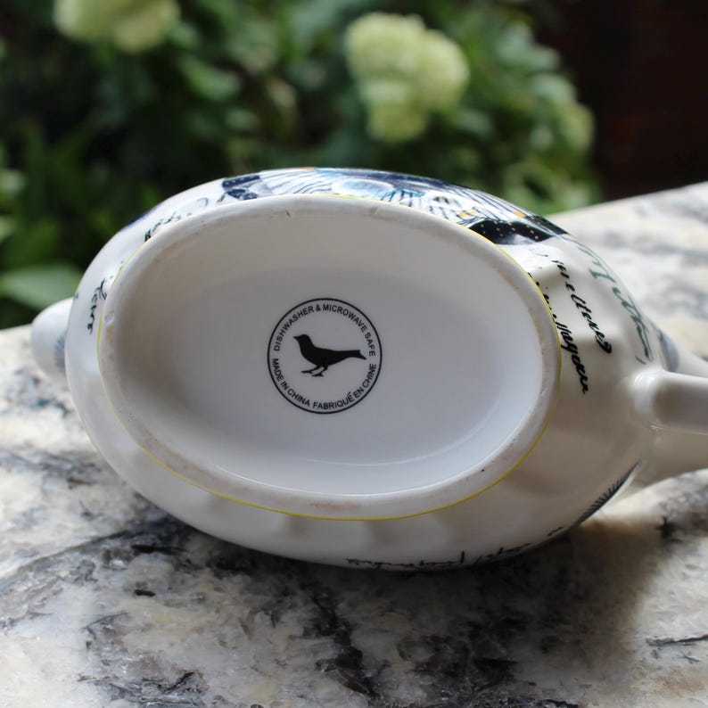 May include: White ceramic teapot with a bird design and black text. The bottom of the teapot has a circular stamp that reads "Dishwasher & Microwave Safe" and "Made in China Fabriqu&eacute; en Chine".