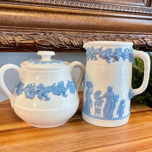May include: A white sugar bowl and creamer set with blue floral designs. The sugar bowl has a lid and both pieces have a delicate floral pattern.