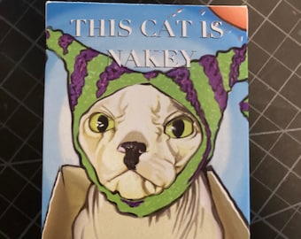 May include: A white cat wearing a green and purple hat with the text "This Cat Is Nakey" and the word "Tarot" below. The cat is in a box with the word "Priority" on the bottom.