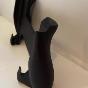 以下が含まれることがあります： 湾曲したデザインの黒いプラスチック製の携帯電話スタンド。スタンドは底に2つのフックと背面に隆起した部分があります。