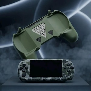 Pode incluir: Uma consola de jogos portátil com padrão de camuflagem e ecrã preto, posicionada abaixo de um acessório de pega de comando em plástico verde-azeitona a condizer, com aberturas de ventilação triangulares e superfície interior texturada.
