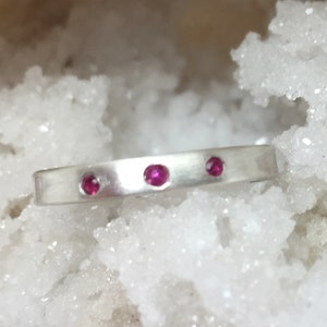 Op de afbeelding: Een zilveren ring met drie kleine roze edelstenen die in de band zijn gezet.