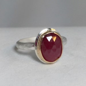 Op de afbeelding: Een zilveren ring met een gehammerde band en een rode edelsteen gezet in een gouden bezel.