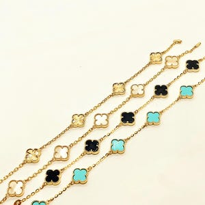 Peut inclure: Bracelets à chaîne dorée avec des breloques en forme de trèfle de différentes couleurs : blanc, noir, turquoise et nacre. Les bracelets sont présentés sur un fond blanc, mettant en valeur leur design délicat.