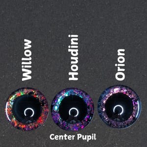 Puede incluir: Tres ojos redondos de vidrio con pupilas negras y detalles de purpurina de colores. Los ojos est&aacute;n etiquetados como "Willow", "Houdini" y "Orion". El texto "Center Pupil" est&aacute; debajo de los ojos.