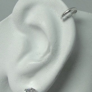 May include: A close-up of a white ear model with a silver hoop earring and a silver stud earring with a clear round stone.