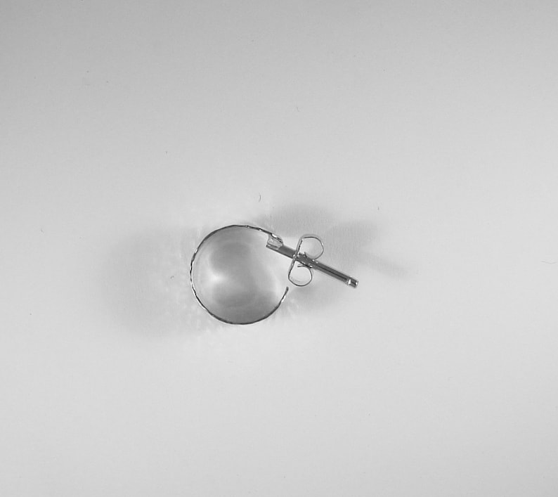 May include: A single silver hoop earring with a post and butterfly clasp. The earring is a half-circle shape, with a textured edge. The earring is set against a white background.