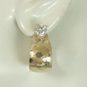 May include: A pair of gold hammered earrings with a single round clear stone in each earring.