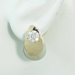 May include: A pair of gold and silver teardrop shaped earrings with a clear round gemstone in the center.