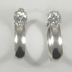 May include: A pair of silver hoop earrings with a single clear cubic zirconia stone on each hoop.