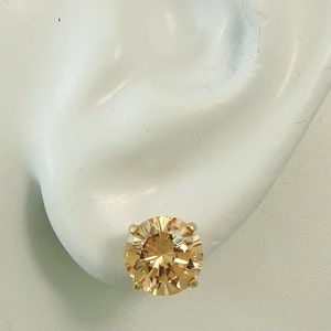 May include: A pair of gold stud earrings with a large, round, champagne-colored gemstone.