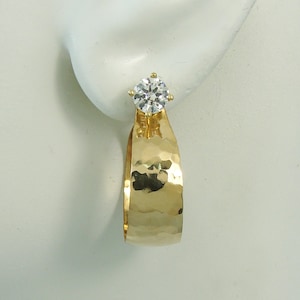 May include: A gold hammered earring with a clear round gemstone.
