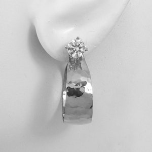 May include: Silver hammered hoop earrings with a single clear round gemstone.