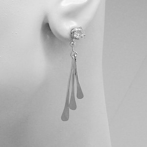 May include: Silver dangle earrings with a single clear crystal at the top and three teardrop-shaped pendants.